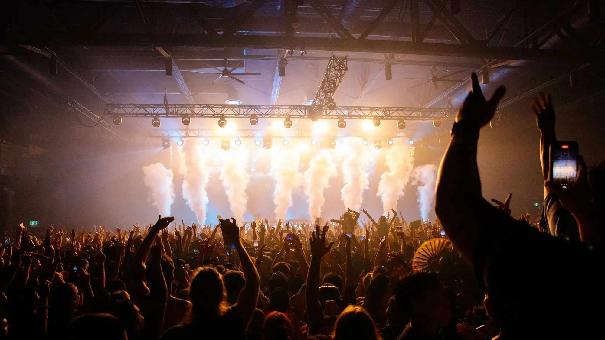 Live concert stage seen from the floor, lighting beams sweeping over the audience.